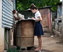Girl in uniform, standing outside using a barrel as a make-shift desk for school work and study
