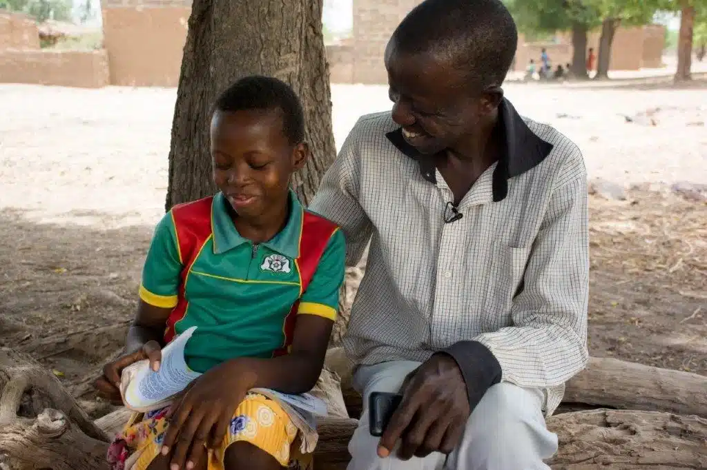 Marina and her father reading a book under a tree.