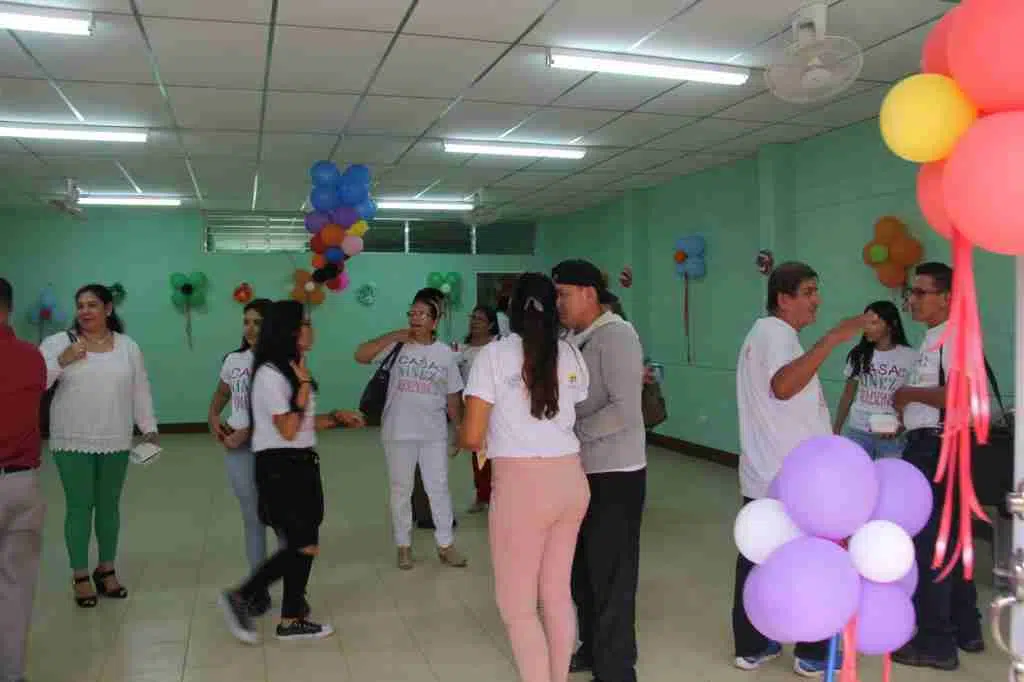 People in a hall talking to each other, balloons are on the walls, People look happy